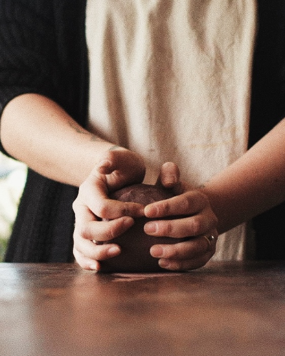 Hands cupping a ball of clay on a wooden table